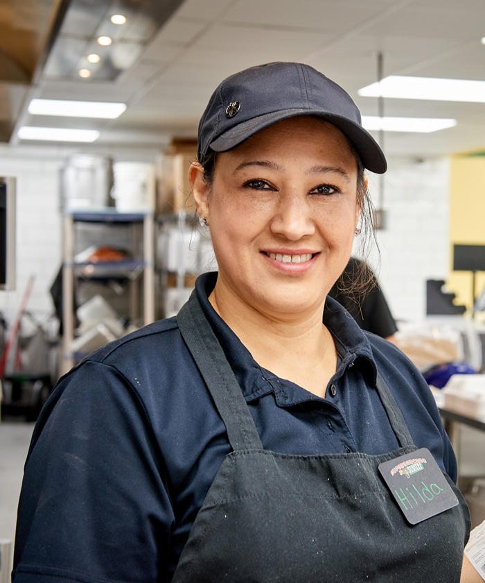 a woman wearing a hat and apron smiling in a Supermercado deli