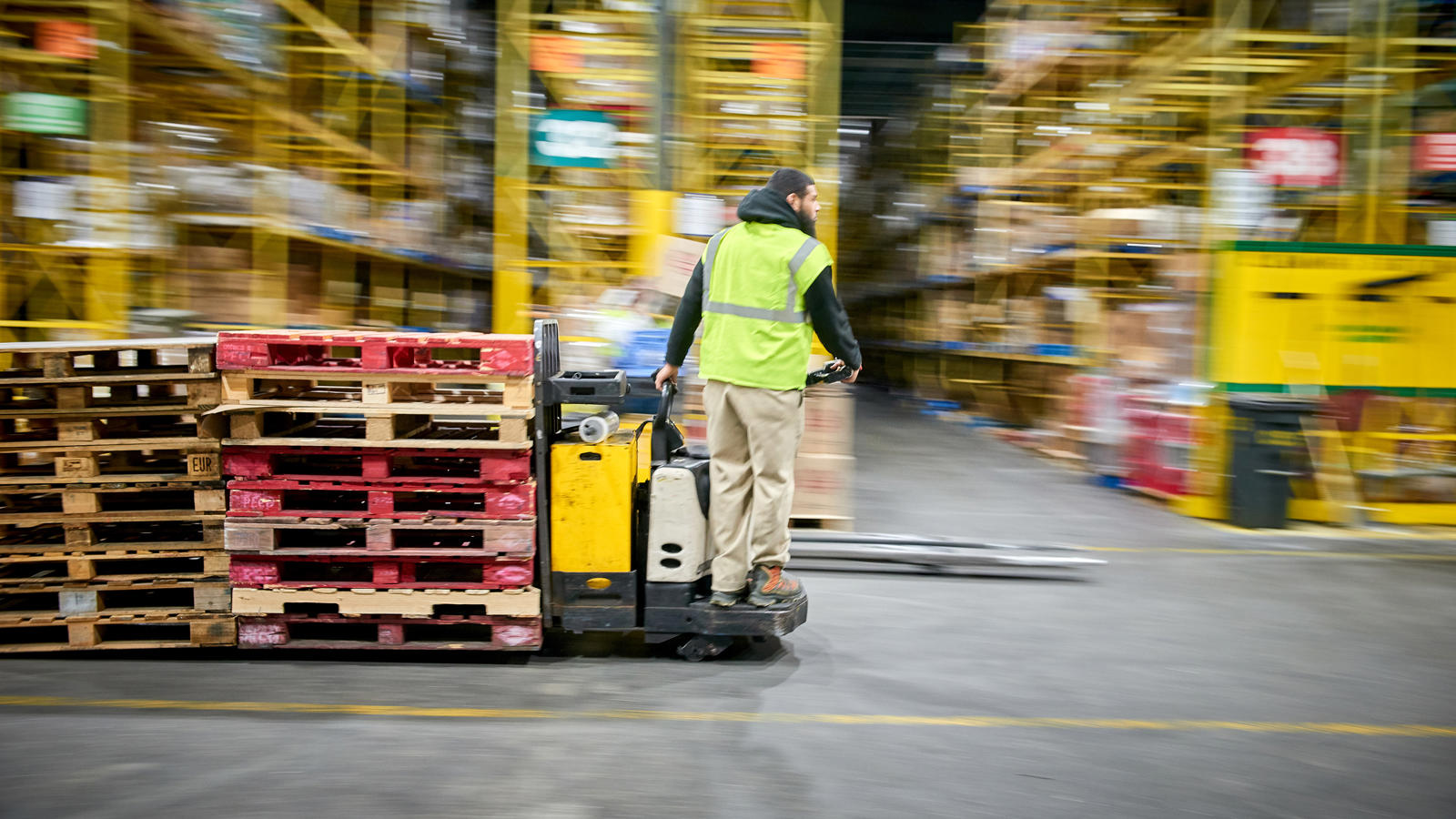 a man in a yellow vest with a forklift in a warehouse