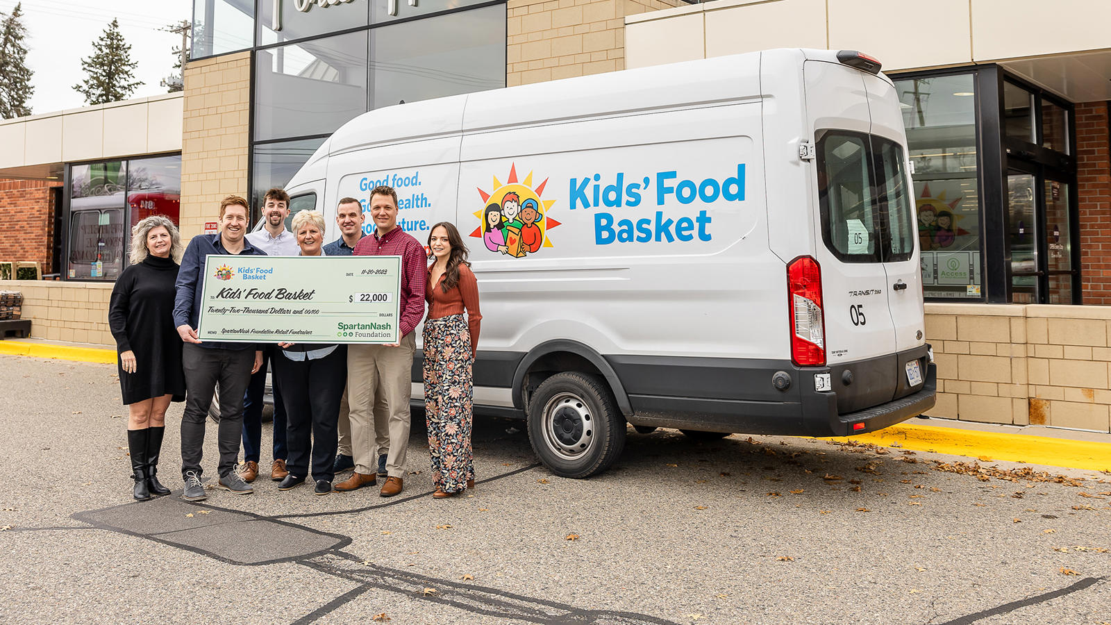 people from SpartanNash and Kids Food Basket holding a large check in front of a white van
