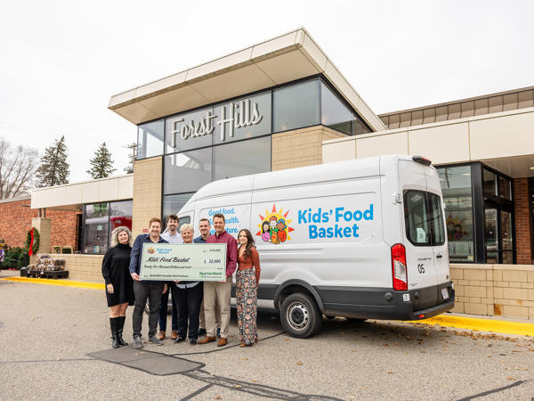 people from SpartanNash and Kids Food Basket holding a large check in front of a white van