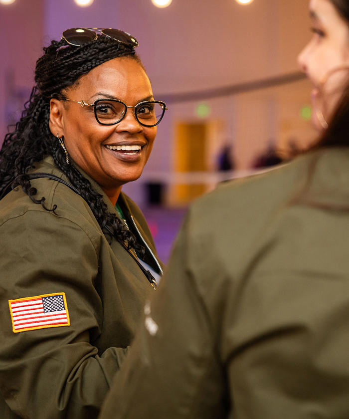 a woman in glasses and a green jacket with a flag on her head for Veterans