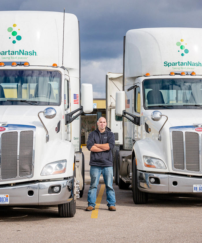 a man standing next to two semi trucks for SpartanNash