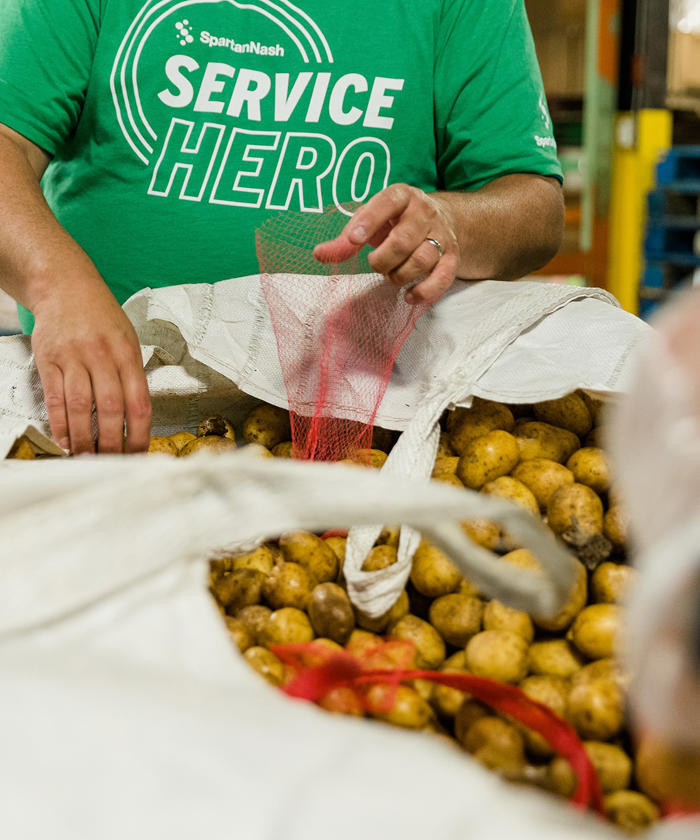 a man in a green shirt sorting potatos for donation