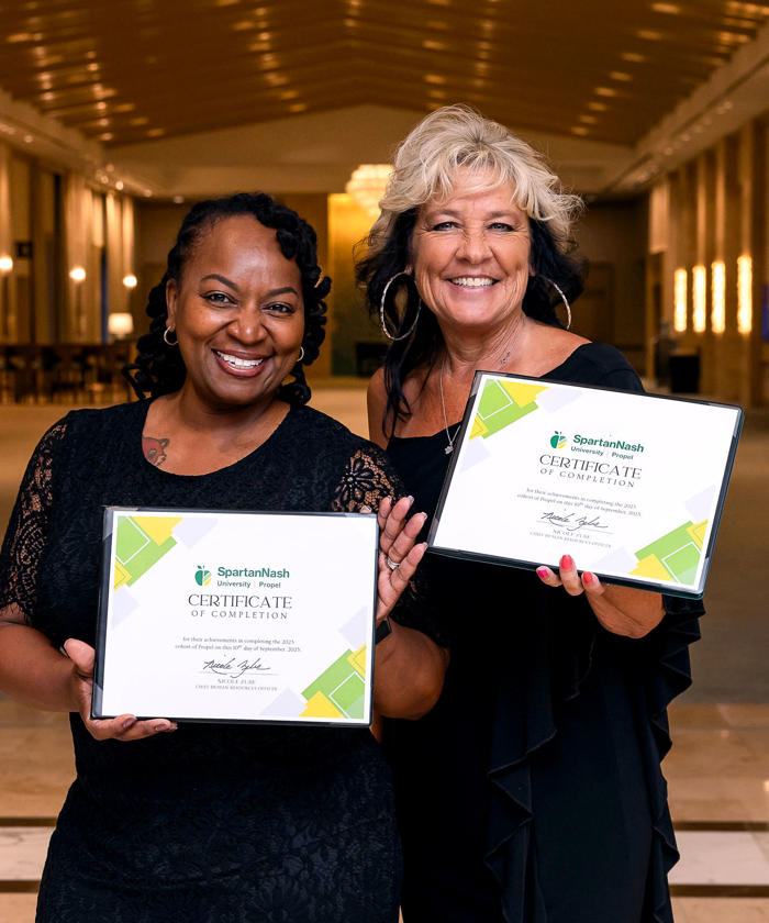 two women holding SpartanNash awards certificates in a hall