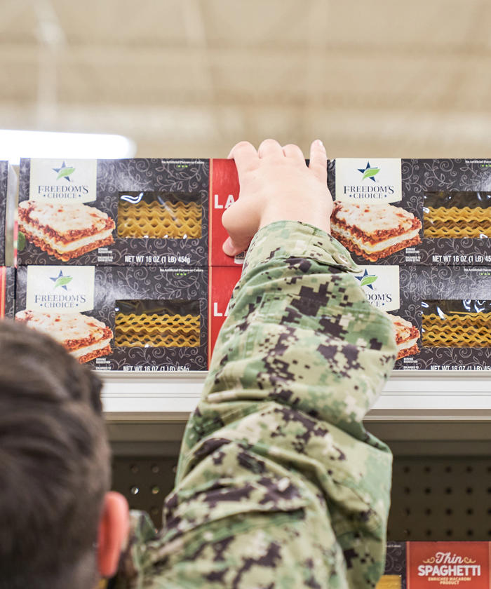 a person in military uniform reaching over a shelf of food